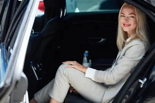 An elegant businesswoman sits in a luxurious car, ready for her personal private driver. Enhance your business trip with our black car service. Book a ride today.