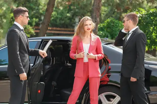 A famous celebrity with bodyguards near a black limo, surrounded by a man and woman in business attire - Roadshow Services.
