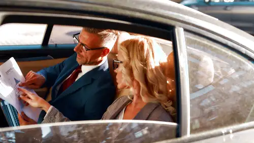 A couple reviewing paperwork in a car, possibly discussing chauffeur service options.