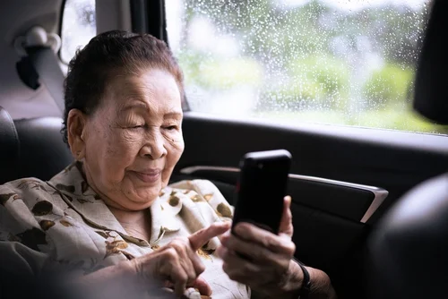 An elderly woman uses her smartphone while riding in reliable transportation to a doctor’s appointment in Houston, highlighting accessible and senior-friendly medical transit services.