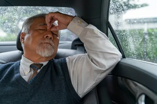 An elderly man rests peacefully in the back seat of a luxury black car, using a private car service for hospital visits in Houston, reflecting comfort and dependable non-emergency medical transportation.