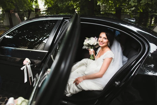 A bride sits in the back seat of a decorated black sedan limousine, smiling with a bouquet, representing Lavish Ride’s Houston wedding limo service.