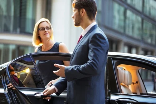 A professional chauffeur opens the door of a black luxury car to greet a businesswoman, representing premium Houston Hobby Airport (HOU) car service.