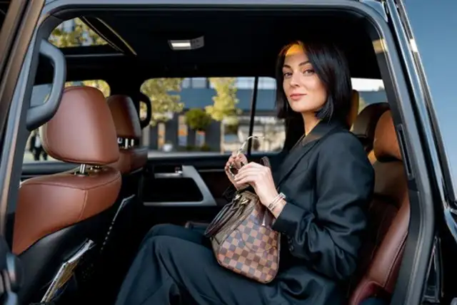 A businesswoman in formal attire sits in the back seat of a sedan limousine, ready to begin a long-distance trip with hourly chauffeur-driven service.
