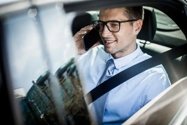 A businessman talks on his mobile phone while seated in the back of a luxury vehicle, using hourly car service.