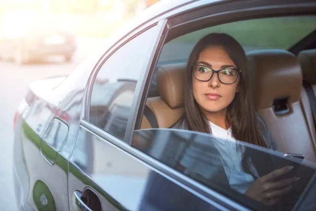A woman in formal attire looks out of the open window of a black luxury car while using the hourly limo service.