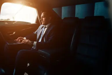 A businessman is focused on his MacBook in the back seat of a black car service during his commute, symbolizing productive and seamless executive transportation.