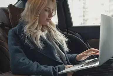 A young woman uses her Mac while receiving stress-free long-distance black car services to travel from city to city.