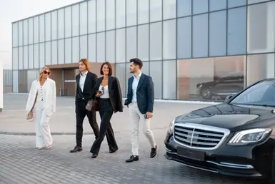 A group of well-dressed men and women exit an office building, preparing to board a black car service for corporate events and group transportation services.