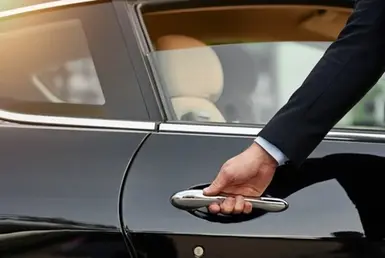 A professional businessman in a suit holds the door handle of a sleek black car, ready for a point-to-point car service or business commute in the city.