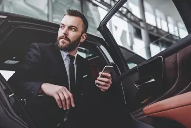 A businessman exiting a chauffeured black car, assisted by a chauffeur, illustrating professional roadshow services.