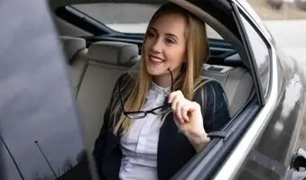 Businesswoman in luxury black car smiling through the window during FBO private airport transportation, symbolizing executive travel, comfort, and professional chauffeur service.