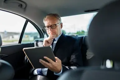 A Elderly businessman in a car using a tablet while enjoying the comfort of Private Chauffeur Service: Elevating Elderly Transportation.