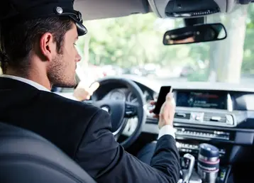 Luxury black Car Driver checking his cell phone waiting for the next road, Symbolising Roadshow Chauffeur Service in Houston show station ride