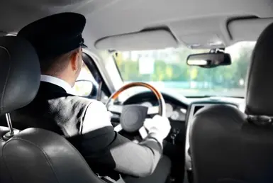 The rear view of a professional chauffeur driving a luxury black limo sedan through Houston symbolizes Lavish Ride’s Houston limousine services.