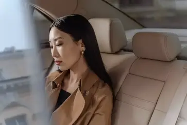 A young woman relaxes in the back seat of a black luxury car driven by a professional chauffeur, representing premium Houston Hobby HOU Airport transportation.