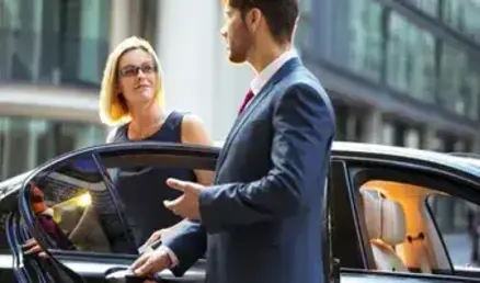 A professional chauffeur opens the door of a black luxury car to greet a businesswoman, representing premium Houston Hobby Airport (HOU) car service.