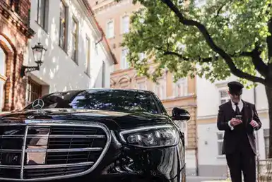 Limousine transfer chauffeur with chauffeur hat, stands by luxury car. Holding Mobile phone in hand. Mercedes Benz S500 S class w223