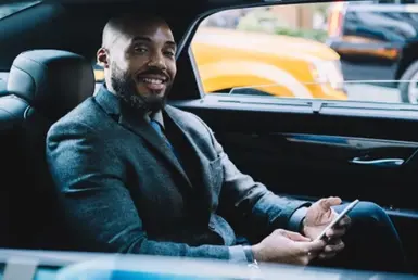 A businessman in formal attire sits in the back seat of a luxury black car as it drives to his destination, representing Corpus Christi Black Car Service.