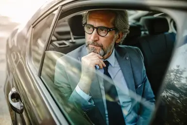 A man in the back seat of a luxury black car, window open, looks out at the scenery, representing Corpus Christi chauffeur services.