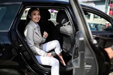A woman in formal attire is about to leave a black luxury car, with the chauffeur holding the door open, symbolizing luxury black car services in Phoenix.