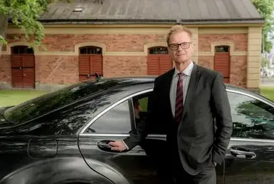 Elevate your travel experience with our chauffeur service - a stylish man in a suit and tie by a black car.