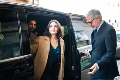 A man and woman entering a black car, availing a private chauffeur service for their airport transfer.
