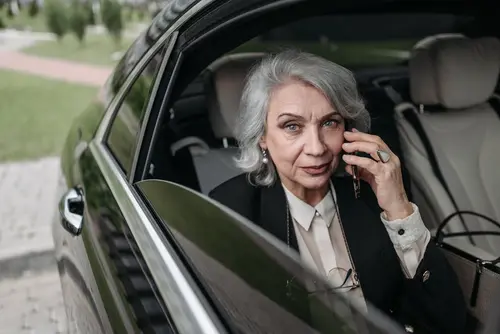 An elderly woman sits in the back seat of a luxurious black car, talking on her phone, symbolizing medical appointment transportation services in Houston.
