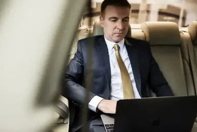 A stylish businessman using a luxury airport shuttle service in a luxury executive Sprinter van reviews his work on his laptop, symbolizing transportation from iah to galveston.