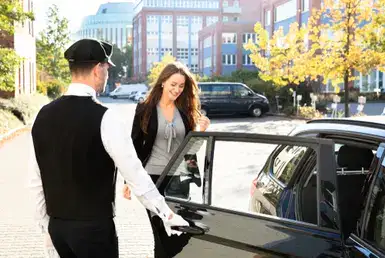 A professional chauffeur of a luxurious black car opens the rear door to help an elegant lady get in. Symbolizing transportation from hobby airport to galveston cruise terminal