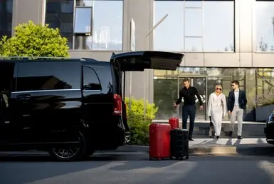 A professional chauffeur assists a group of passengers by transferring luggage from Houston Hobby Airport to a luxury van, representing Lavish Ride’s Galveston Airport transportation.