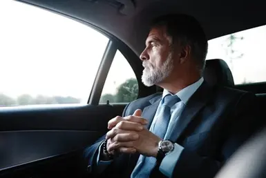 Businessman on black suit sitting in a black car on the way to meeting, symbolizing Houston Executives Hourly Chauffeur Service.
