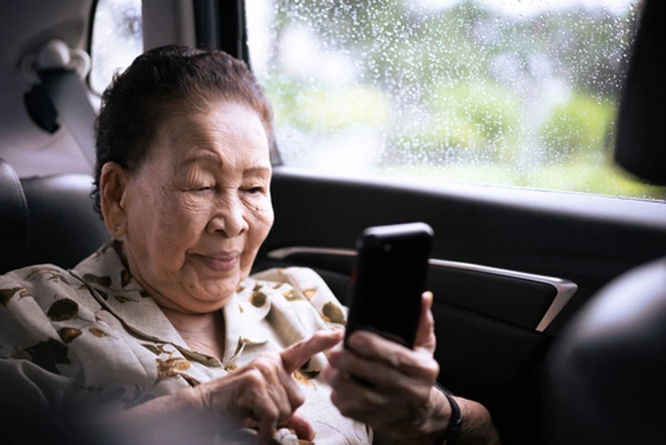 Elderly woman happily video calling in a private car with a chauffeur. Non-Emergency Medical Transportation.