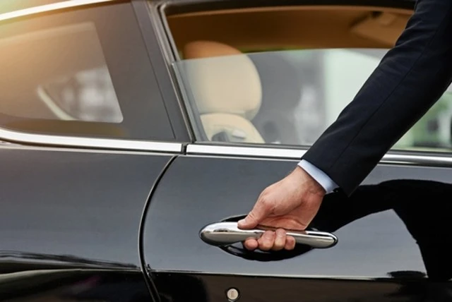 A professional businessman in a suit holds the door handle of a sleek black car, ready for a point-to-point car service or business commute in the city.