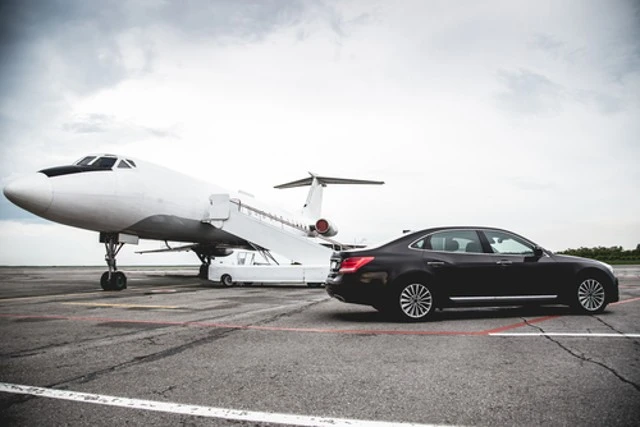 A private chauffeur service with a black luxury car is waiting for the client near a private Jet on the runway at Airport