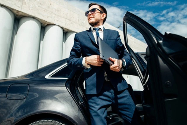 A fashionable businessman coming out of a Luxury car used black car service.