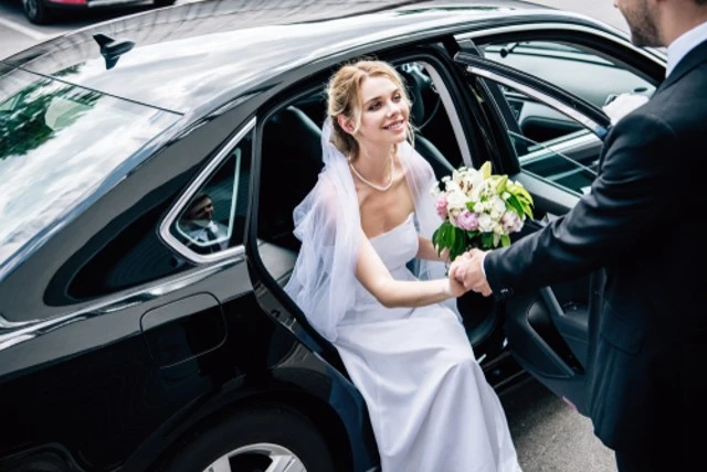 Chauffeur help to attractive and smiling bride with bouquet, bride use limo service for wedding.