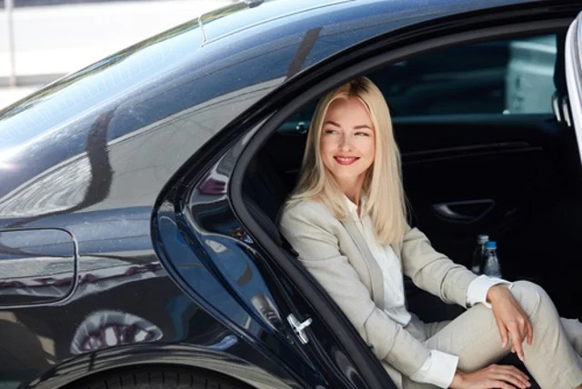 side view of the attractive business lady sitting inside a luxurious car, waiting for a personal private driver, a business trip concept.