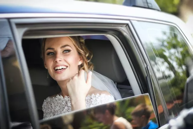 A happy bride in a white wedding dress after riding a luxurious black car service, is getting ready to start her new journey