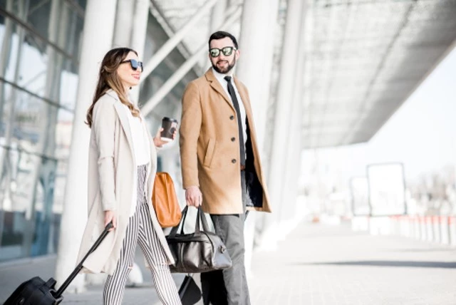 Business couple in coats walking out of the airport with luggage during the business trip and go to Airport Limo Service.