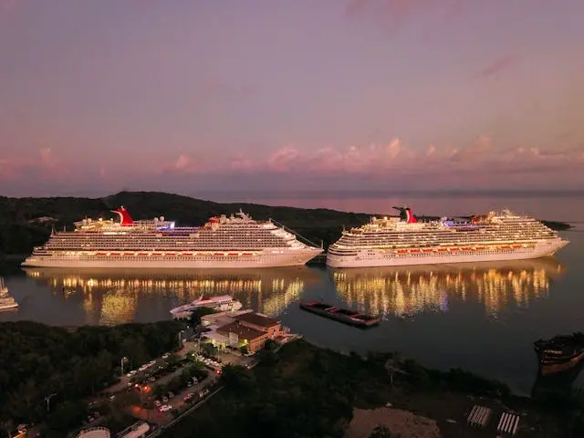 A picture of two huge passenger ships in a port at night, their lights on and reflecting a beautiful image on the surface of the water.