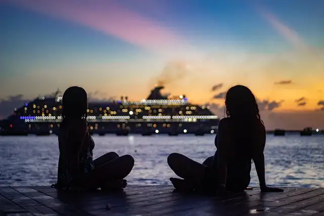 Two women enjoying their time at dusk in a port opposite a cruise ship in the picture